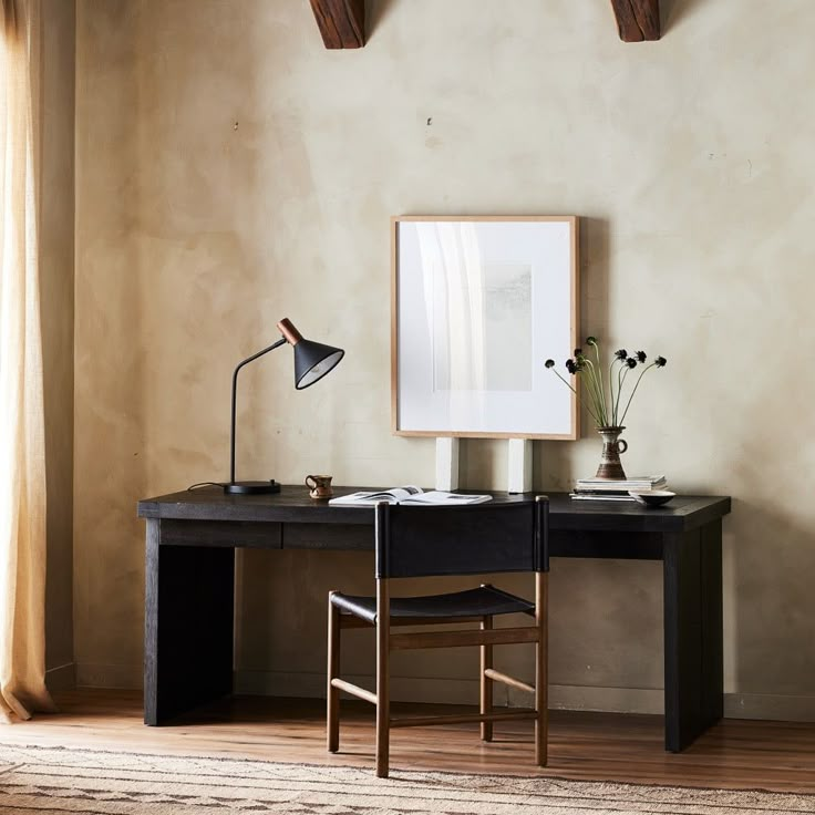 a desk with a lamp and pictures on the wall above it, in front of a window