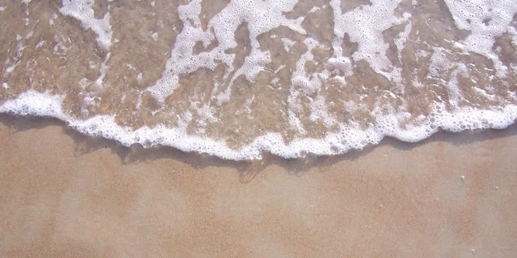 an aerial view of the ocean with waves coming in to shore and people walking on the sand