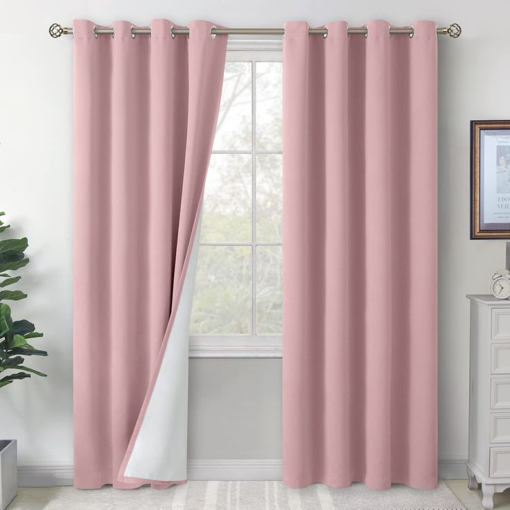 a pink curtain hanging in front of a window with a white rug and potted plant