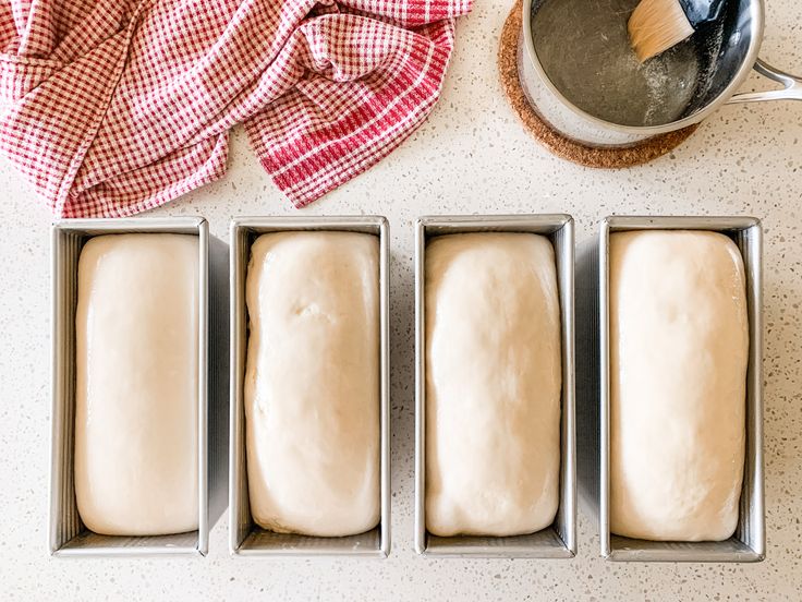 four loafs of bread sitting in pans next to a red and white towel