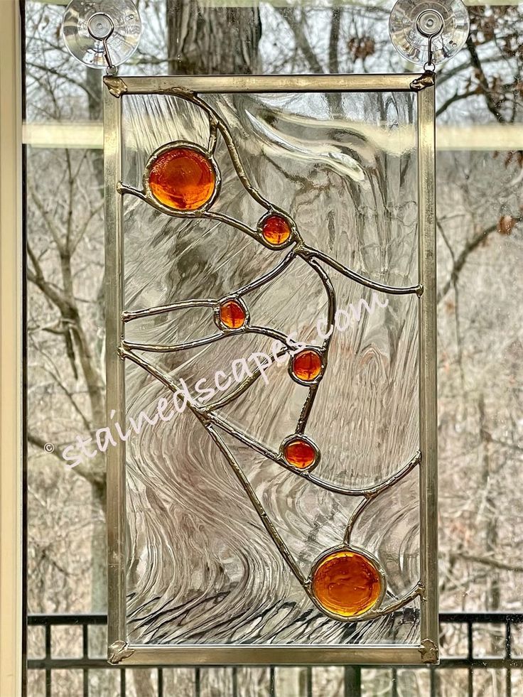 a stained glass window with trees and branches in the background, on a porch railing