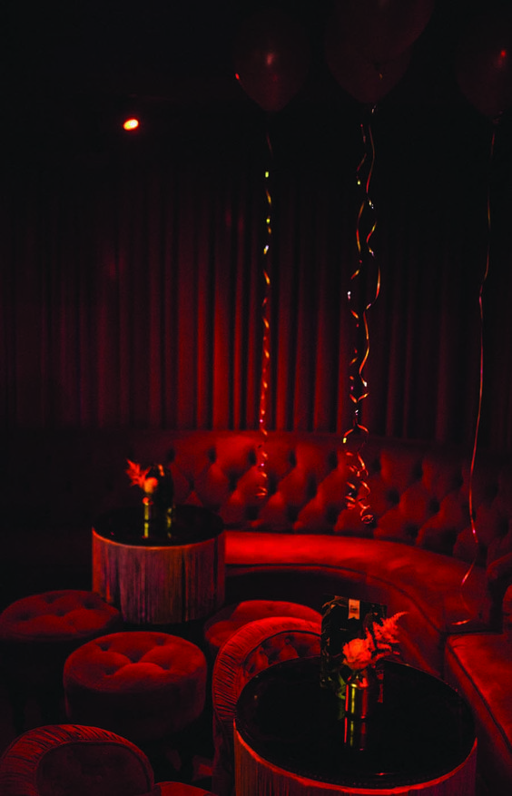 a room with red couches, round tables and balloons hanging from the ceiling at night