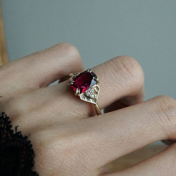 a close up of a person's hand wearing a ring with a red stone