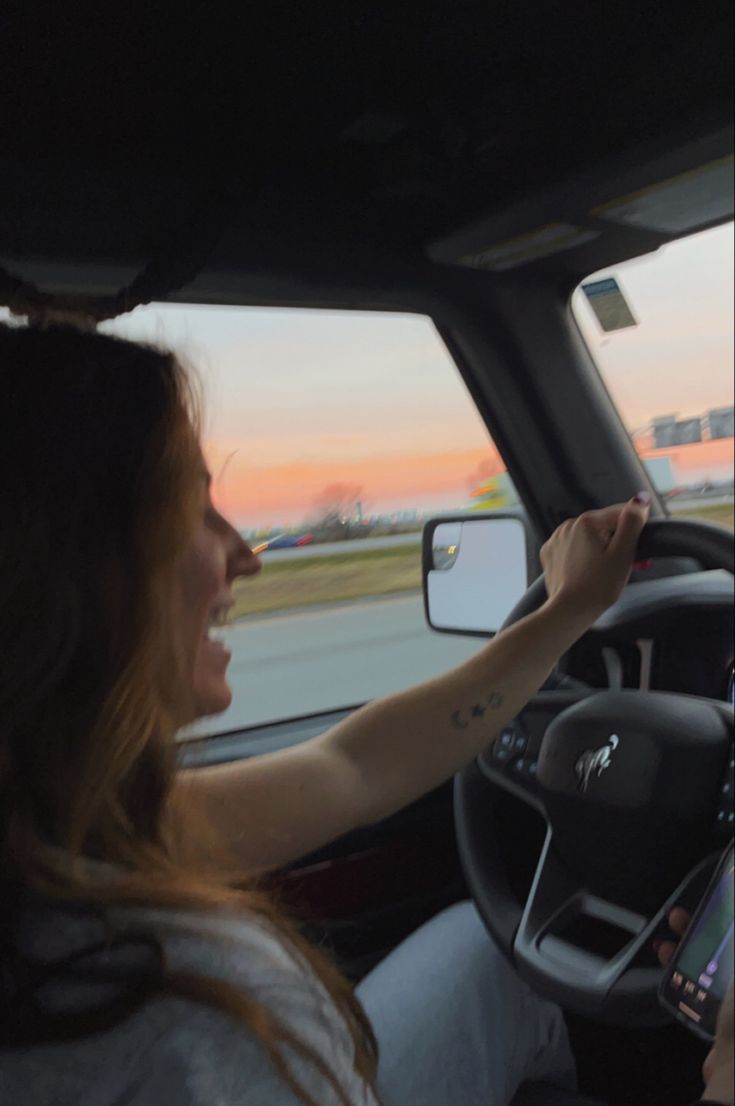 a woman is driving in her car with the sun setting