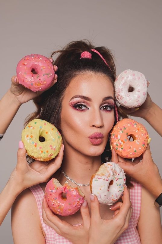 a woman holding five donuts in front of her face and four behind her head