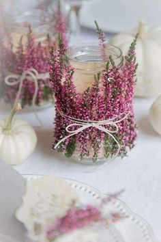 purple flowers are in a glass jar on a white tablecloth with plates and napkins