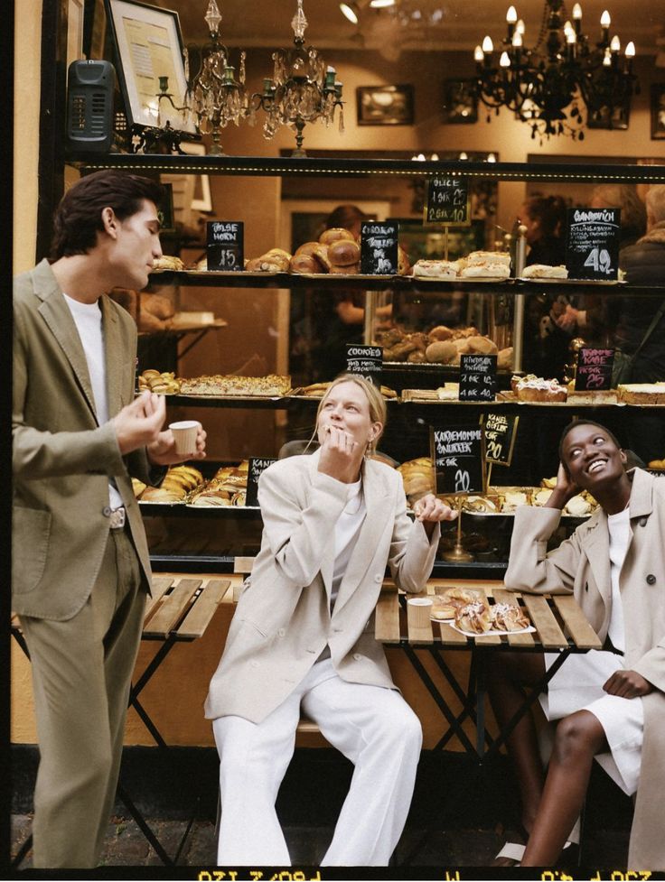 three people sitting at a table in front of a bakery