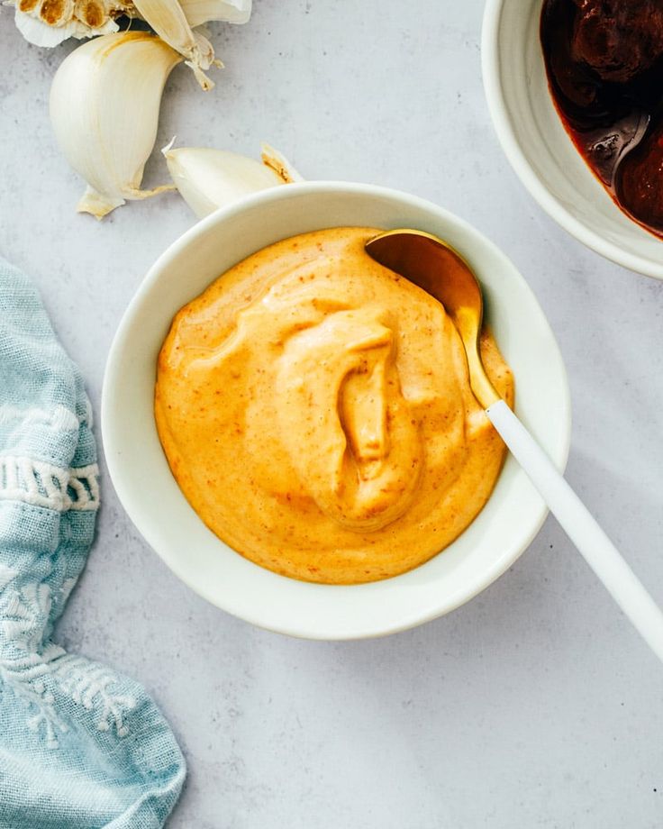 a bowl filled with peanut butter next to garlic and an onion on a white table