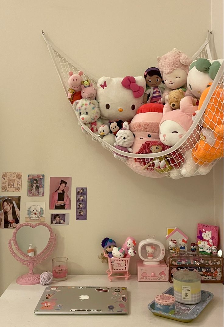 a hammock filled with stuffed animals on top of a white desk next to a laptop