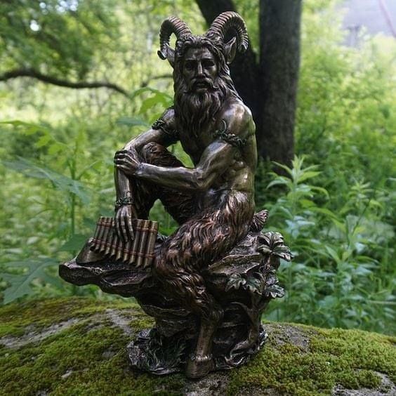 a statue of an old man sitting on top of a moss covered rock in the woods