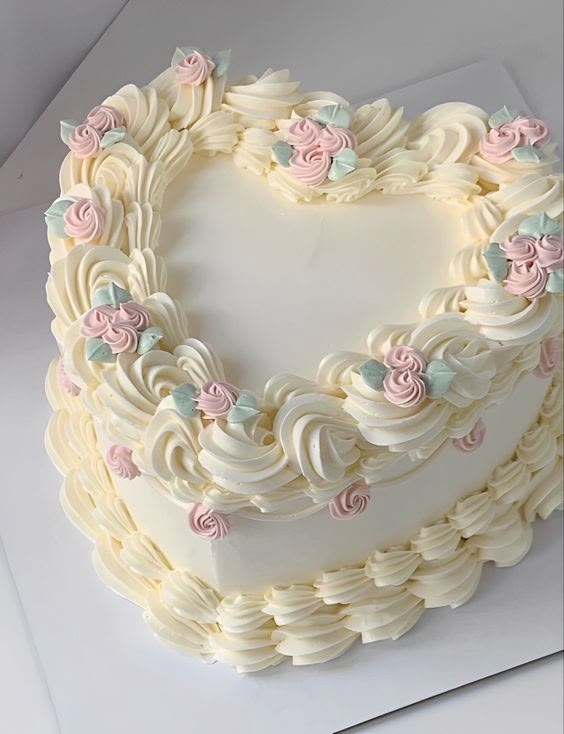 a heart shaped cake with white frosting and pink flowers on it's edges