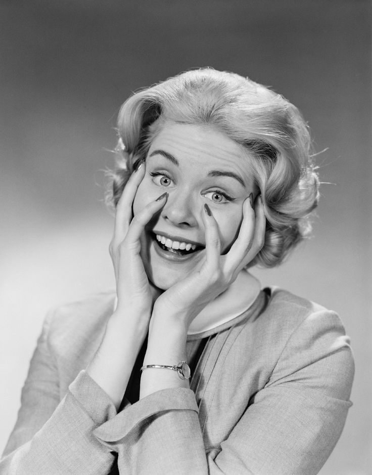 an old black and white photo of a woman with her hands on her face smiling