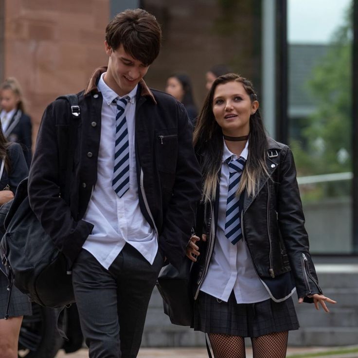 two young people dressed in school uniforms walking down the street