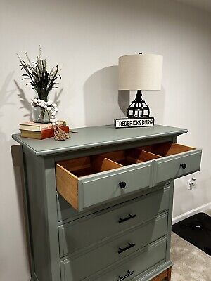 a green dresser with drawers and a lamp in the corner on top of a carpeted floor