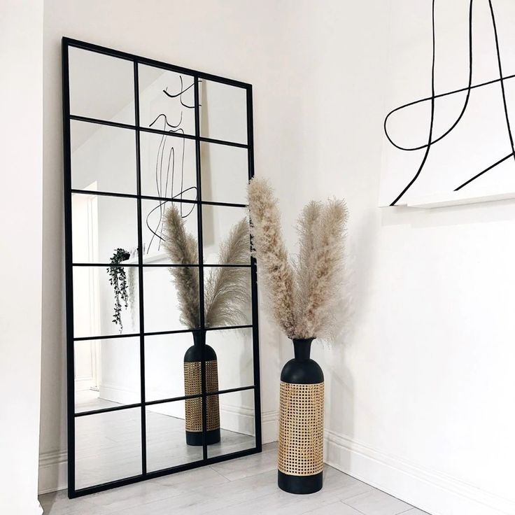 two vases with dry grass in front of a mirror on the wall next to it