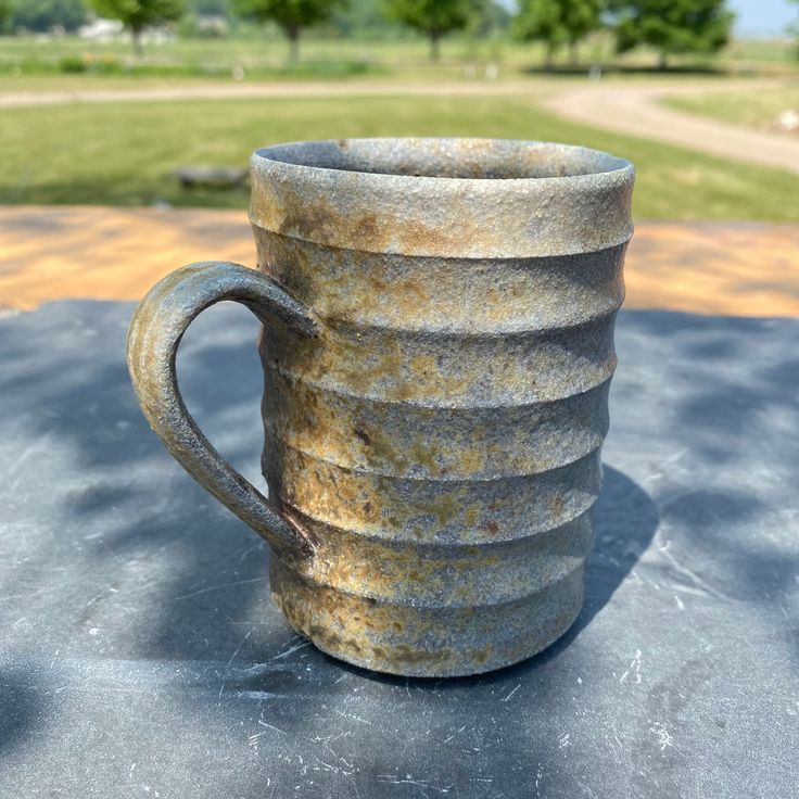 an old coffee cup sitting on top of a cement table in front of a grassy field