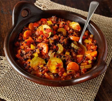 a bowl filled with chili and vegetables on top of a wooden table next to a spoon