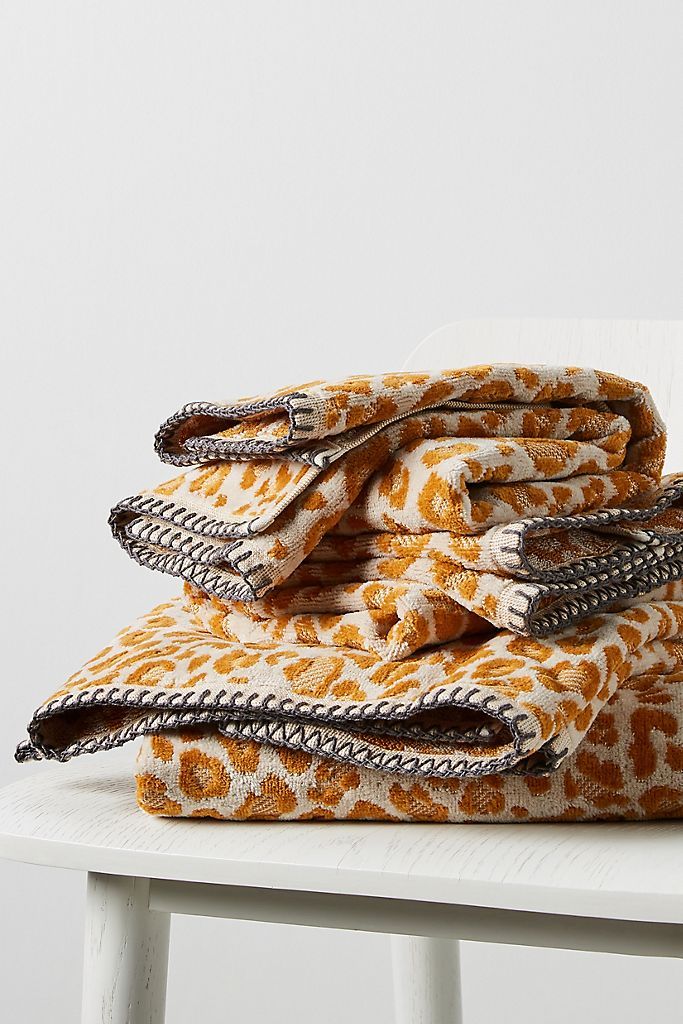 three folded towels on top of a white chair with an orange leopard print covering it