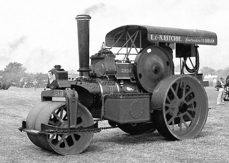 an old steam engine sitting in the middle of a field with people standing around it