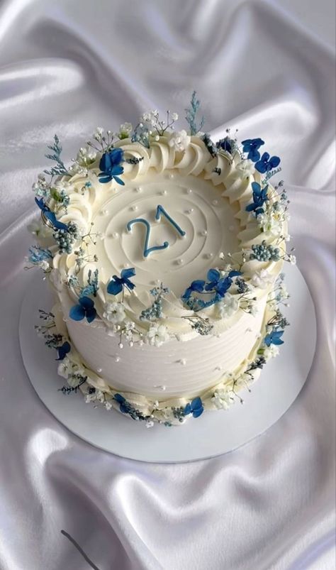 a white cake with blue flowers on it sitting on top of a cloth covered table