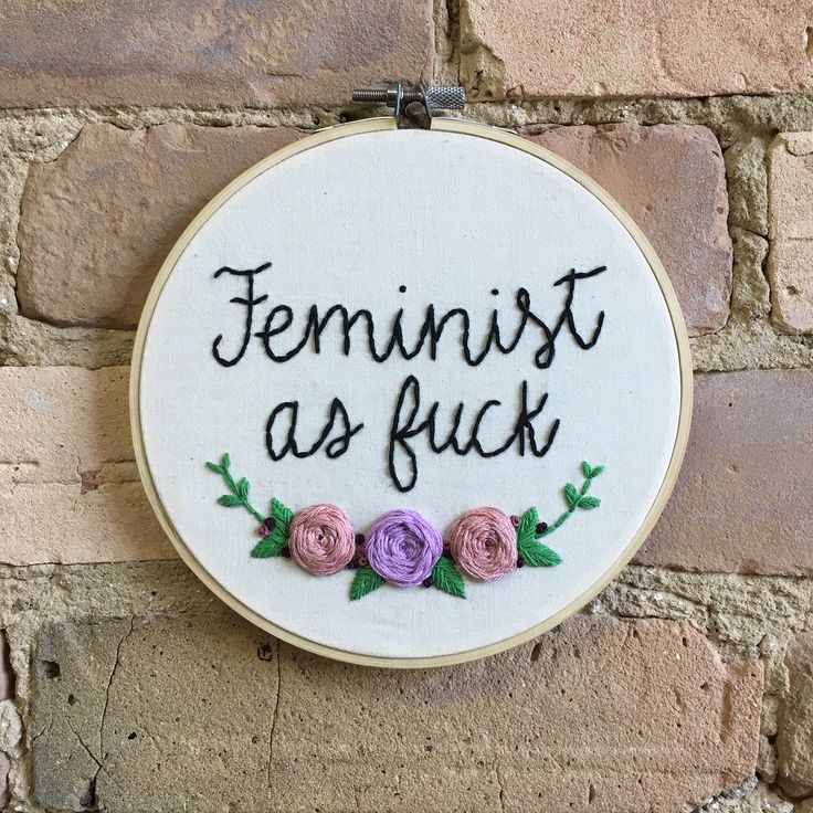 a hand embroidered sign that says feminist as fock with three flowers on it hanging on a brick wall