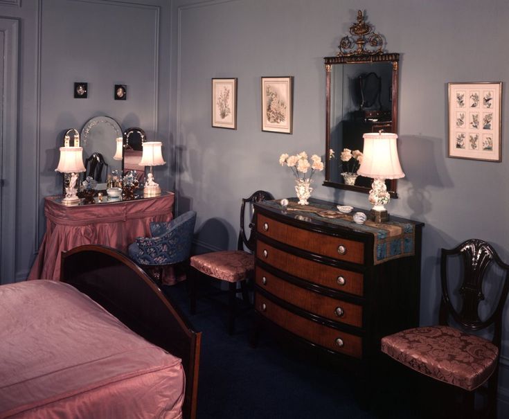 a bedroom with blue walls and pink bedding is pictured in this image, there are two lamps on either side of the dresser