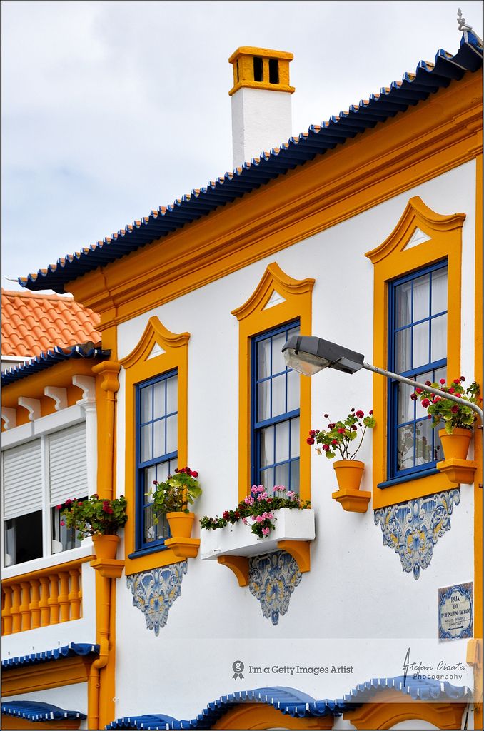 an orange and white building with blue trim on the windows has potted plants in front of it