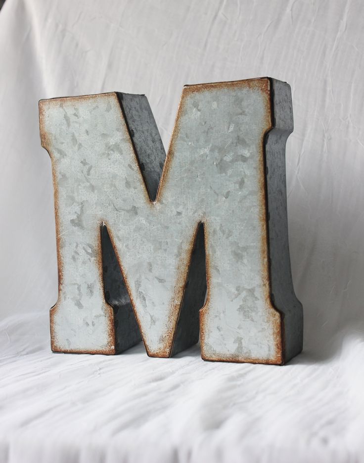 the letter m is made out of metal and has rusted paint on it's sides