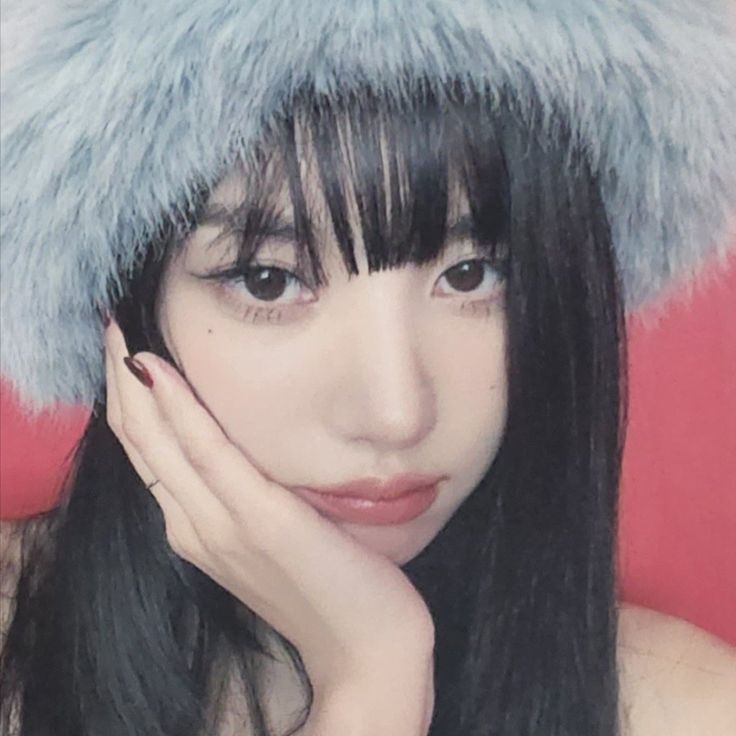 a woman with long black hair wearing a fur hat and posing for a photo in front of a red background