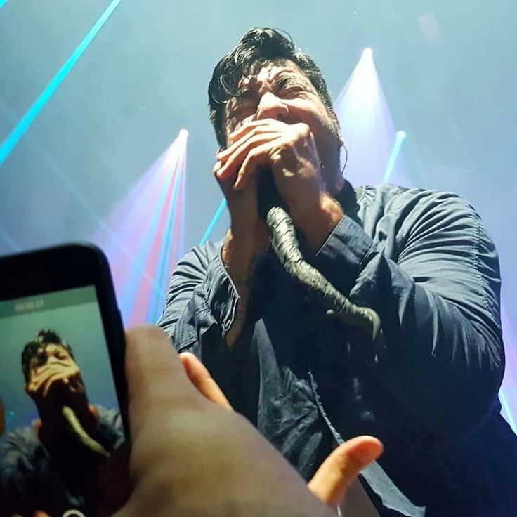 a man holding a snake in front of his face while taking a photo with a cell phone