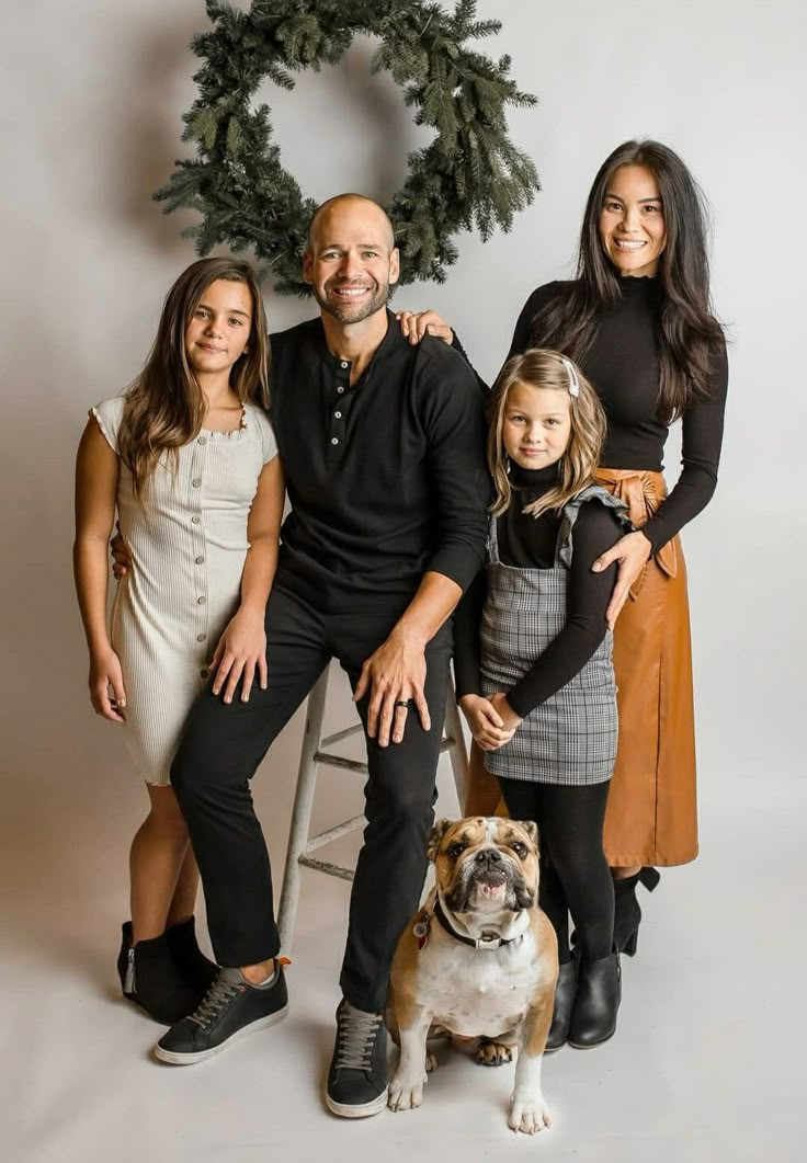 a family posing for a photo with their dog and christmas wreath in front of them