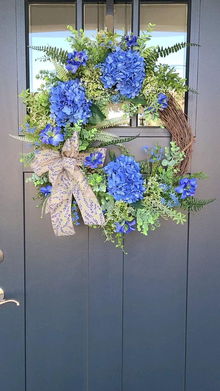 a wreath with blue flowers and greenery hangs on the front door's side