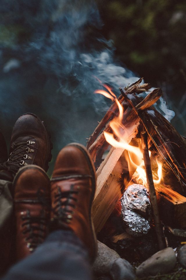 a person sitting in front of a campfire with their feet on the firewood