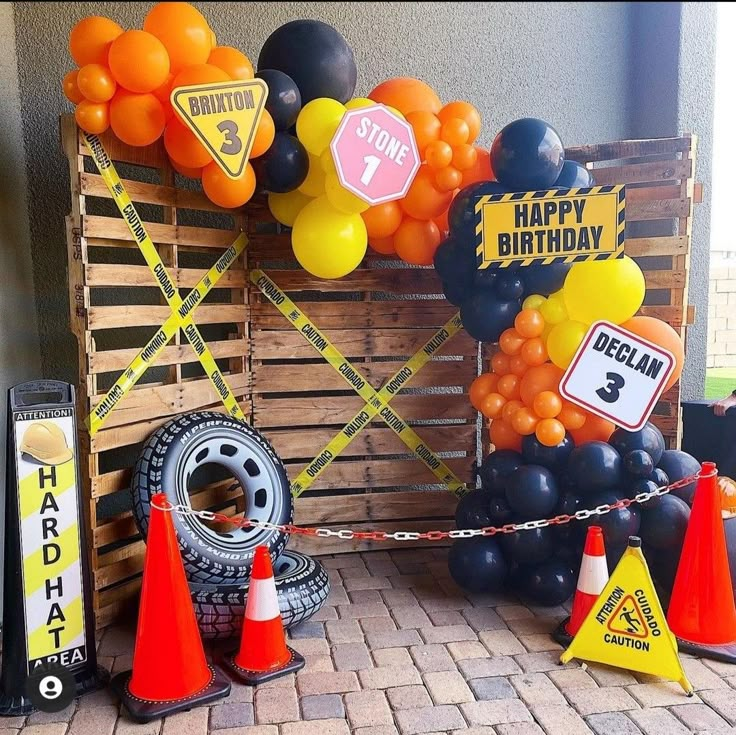 a birthday party with orange and black balloons, traffic cones, and road signs on display