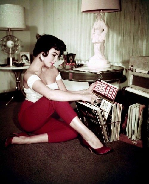 a black and white photo of a woman sitting on the floor with records in front of her