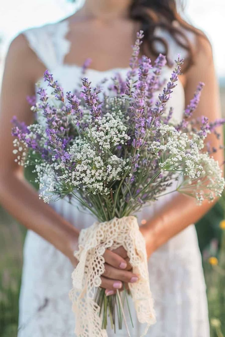 a woman in a white dress holding a bouquet of lavenders with lace on it