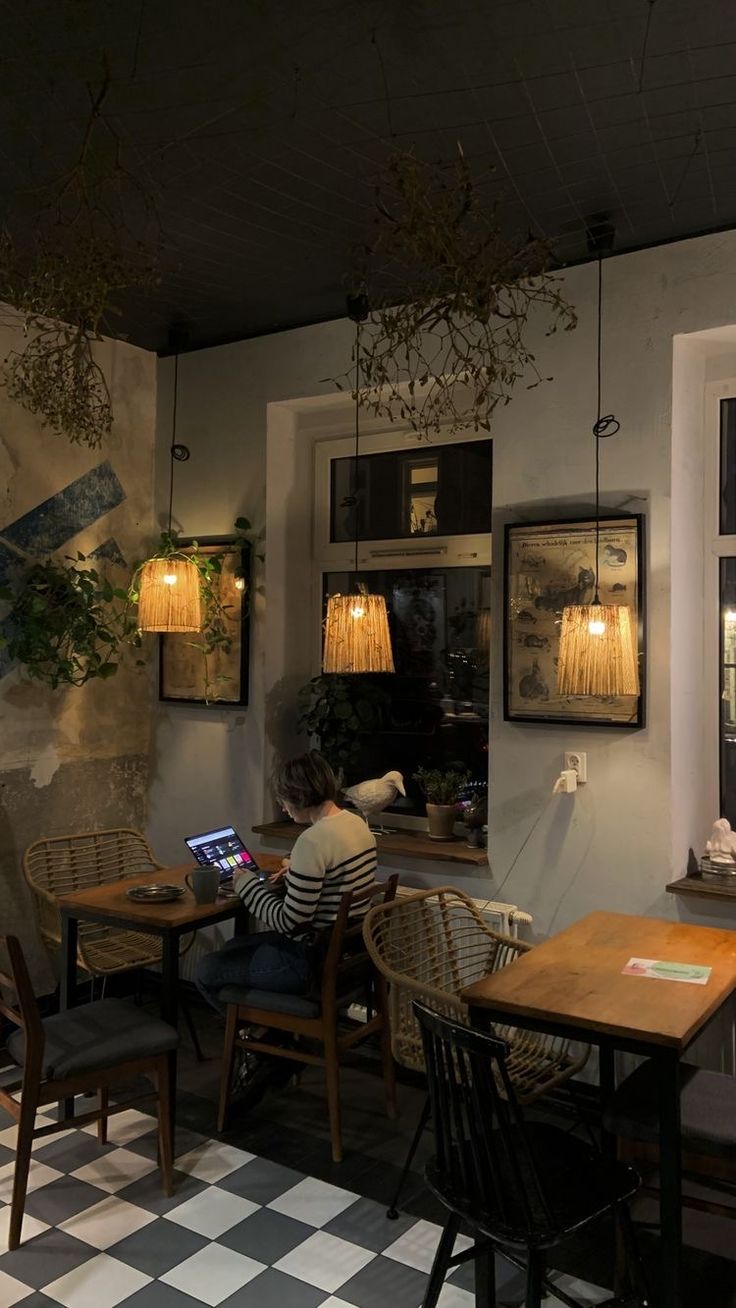 a man sitting at a table with a laptop computer in front of him and some plants hanging from the ceiling