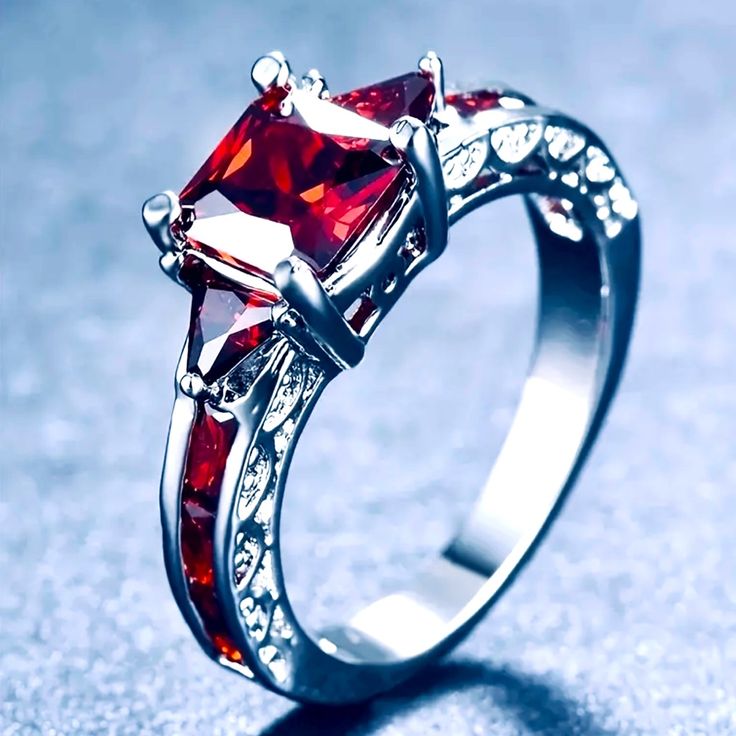 an engagement ring with two princess cut red stones on the sides, set in white gold