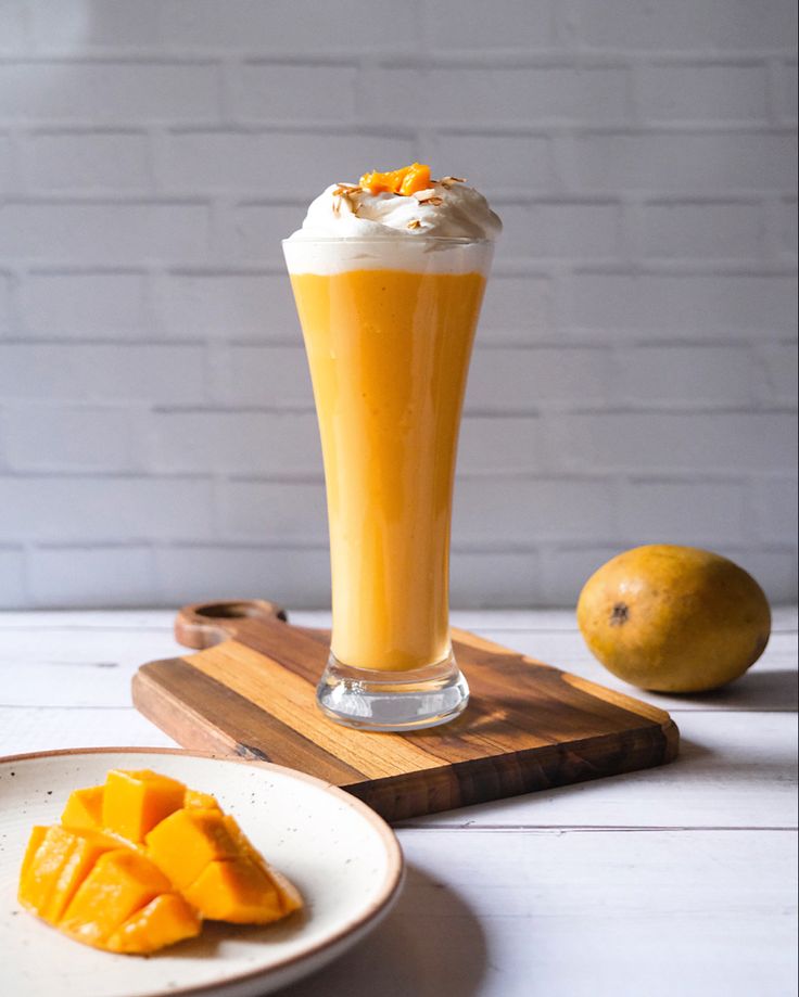 a glass filled with orange juice next to sliced mangoes