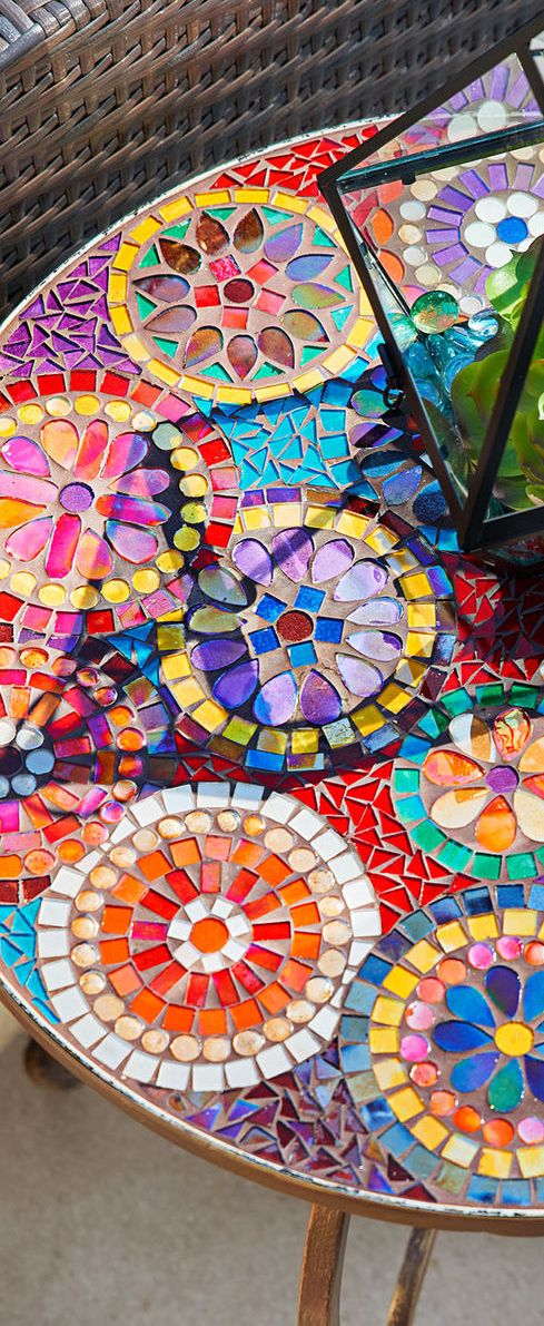 a table that has some kind of colorful design on it, with a glass vase sitting on top