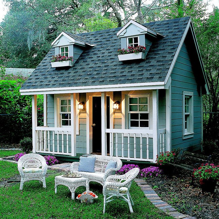 a small blue house with white wicker furniture in the front yard and landscaping around it