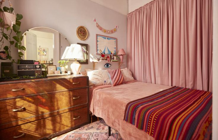 a bedroom with pink curtains and striped bedspread in front of a mirror on the wall