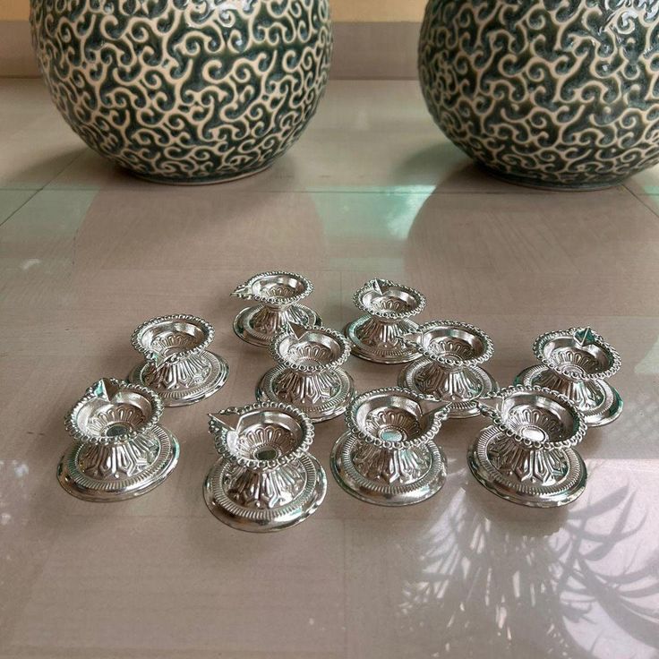 there are many small silver dishes on the table next to two vases and one is empty