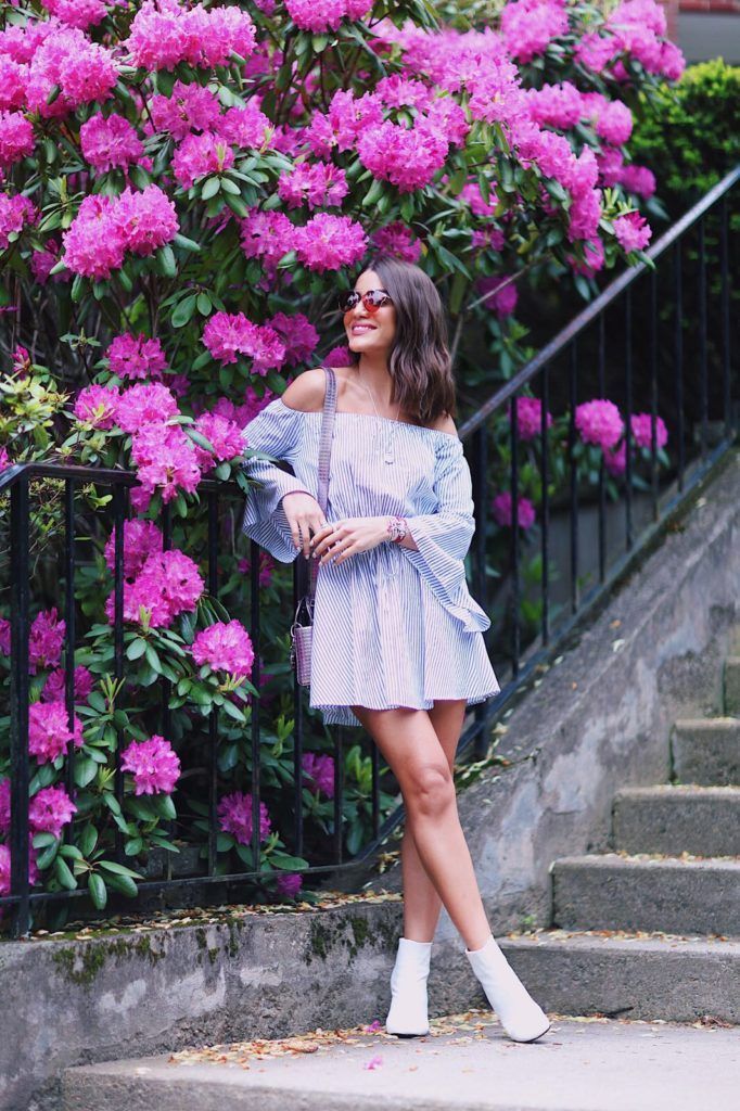 a woman standing in front of pink flowers wearing white boots and an off the shoulder dress