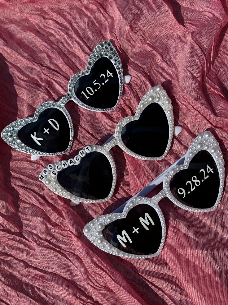 three heart shaped sunglasses with the names and date on them, sitting next to each other