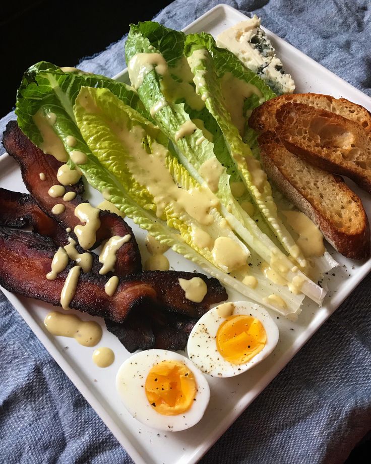 a white plate topped with bacon, lettuce and eggs next to toasted bread