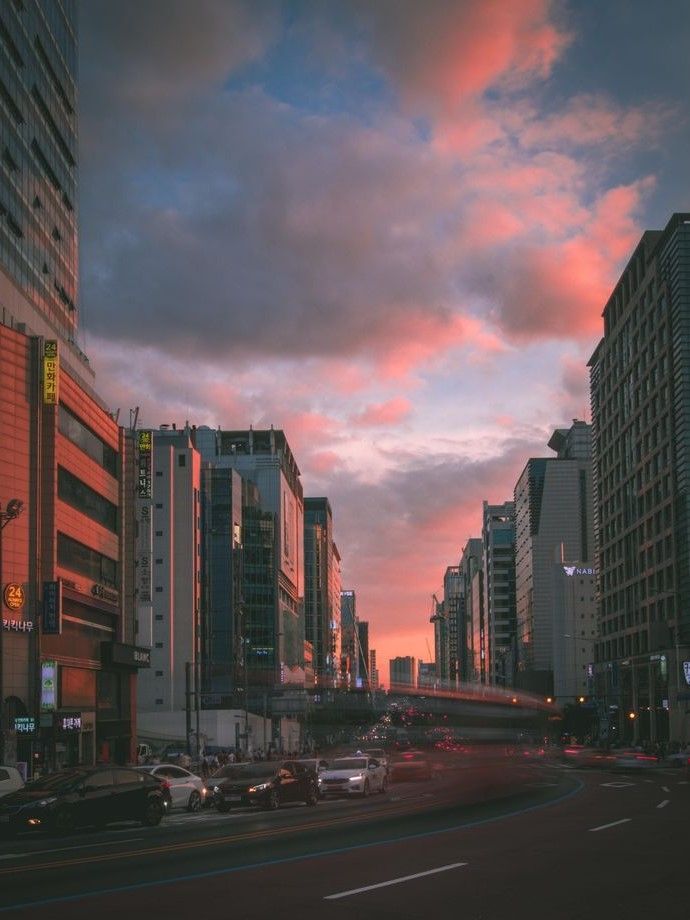 a city street filled with lots of tall buildings under a cloudy blue and pink sky