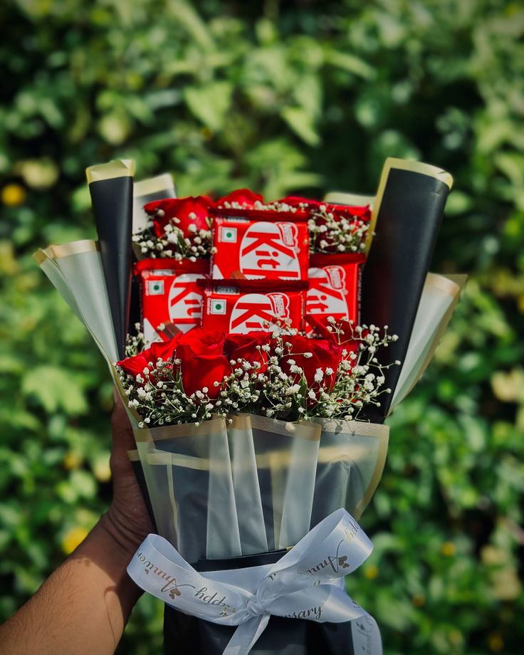 a person holding a bouquet of red and white chocolates in front of green bushes