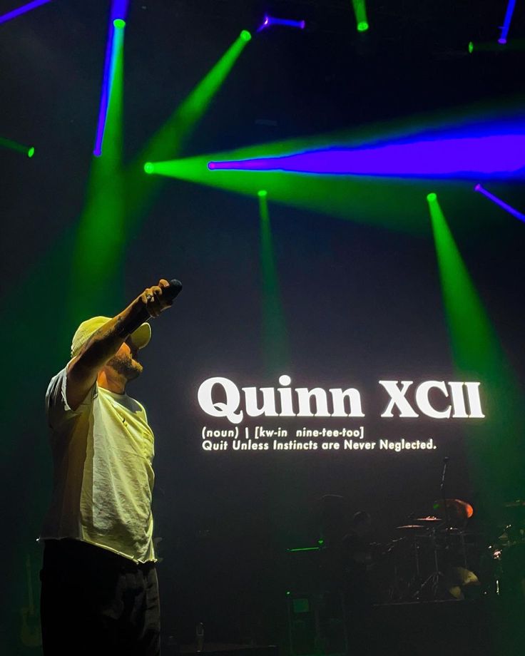 a man standing on top of a stage next to green and purple lights in the dark