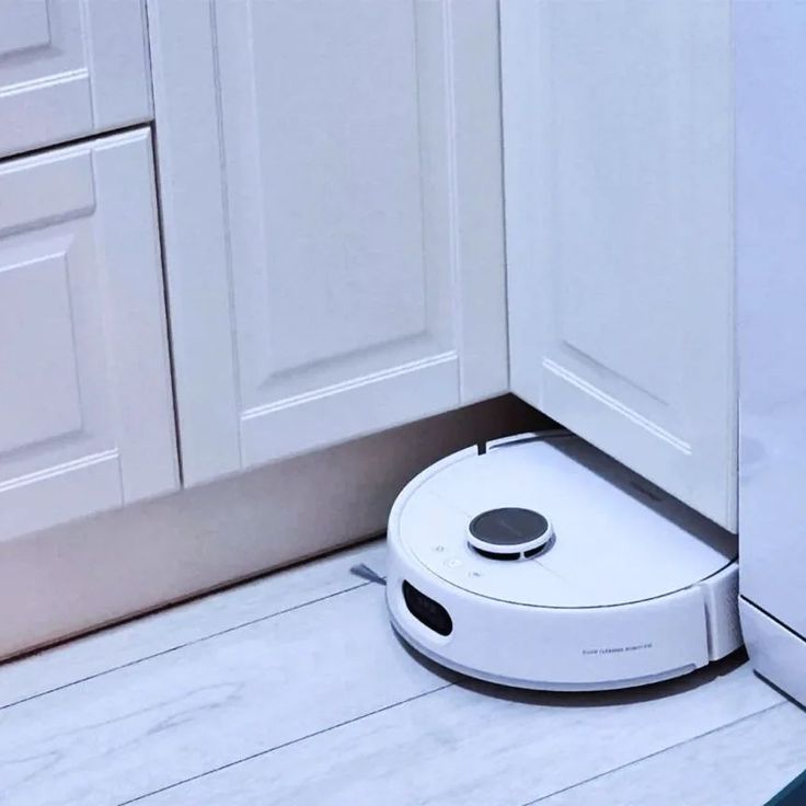 a robotic vacuum is sitting on the floor in front of white cabinets and cupboards